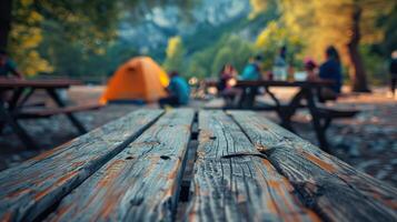 Blurred background of people camping in the forest with wooden picnic tables and a tent, capturing the essence of an outdoor adventure. photo