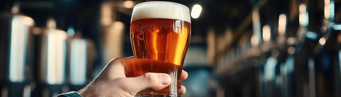 A closeup of a hand holding a frosty craft beer glass, the beers rich amber color highlighted, against a softfocus, industrial background, wide negative space for editorial content photo