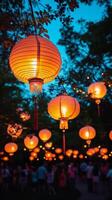 Brightly lit Chinese lanterns hang from trees in night garden. Mid-Autumn festival. Vertical banner photo