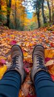 View from first person perspective of legs in boots on path covered in autumn leaves. Fall, vertical photo
