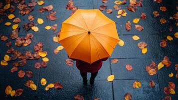 Top view of person under a yellow umbrella held by hands, with autumn fallen leaves on the sidewalk photo