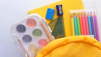 Top view of yellow backpack with different colorful stationery on table. video