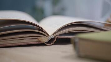 An open book with its pages gently turning rests on a wooden table in the breeze video
