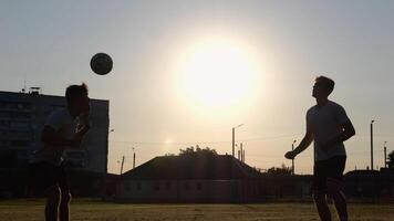Silhouette of professional footballers kicking soccer ball with their heads on stadium at sunset. Two sportsmen showing tricks with ball while passing it to each other at field. Freestyle football photo