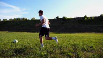 Professional footballer in uniform shows tricks with ball while running at green field. Sportsman kicks ball during jogging at meadow on sunny day. Young man training at stadium. Freestyle football photo