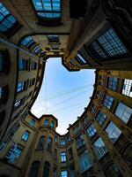 A dramatic upward view of a historic courtyard with curved architecture, emphasizing the symmetry and intricate details of the building against a clear blue sky. The image captures the unique photo