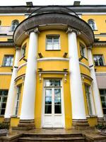 A detailed view of the grand yellow facade of a classical building in St. Petersburg, featuring prominent white columns and elegant architectural details. The symmetrical design and bright color photo