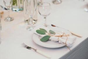 Table setting with napkin on empty white plate, wineglasses and cutlery on table, copy space. Place setting at wedding reception. Table served for banquet photo