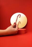 The hand of a young girl with a red manicure holds a candy cane. Cinnamon stick is reflected in a round mirror near a small round stage. photo