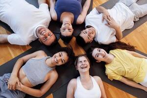 Multi-racial smiling people lie on mats after doing yoga at a fitness club. A group of young athletes relax and rest after physical exercises in the gym. photo