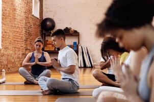 A group of multiethnic athletes sit on mats and meditate. The end of fitness classes and relaxed people in sports clothes in the lotus position in the gym. photo