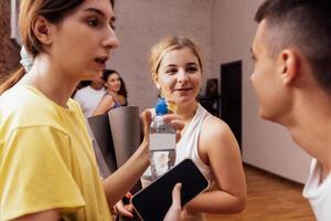 A group of multiethnic athletes roll up mats after yoga classes. The end of fitness classes and talking relaxed people in sports clothes in the gym. photo