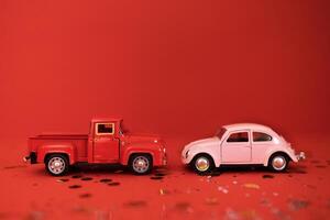 Two toy cars on a red background with glitters and confetti. A red truck and a pink passenger machine stand opposite each other. photo