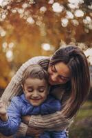 Young happy family, mother and little son child walking in autumn forest, kid holding yellow tree leaf in hand photo