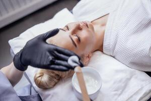 Cosmetologist hands in black gloves hold wooden spatula for applying cream photo