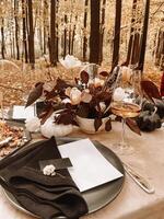 Table serving outdoors in the autumn forest. Black plate and napkin, card, fork, glass of champagne. Nuts and cheese on a plate for snacks. photo