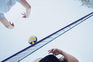 Volleyball game in summertime. Extreme bottom view of the net, multi colored ball and two players. photo