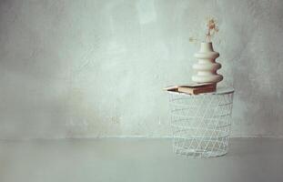 Book and dried twig in ceramic vase on white metal round bedside table against beige concrete wall photo