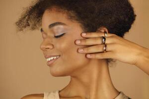 Profile of smiling afro american woman demonstrating rings on her fingers, keeping hands at face photo