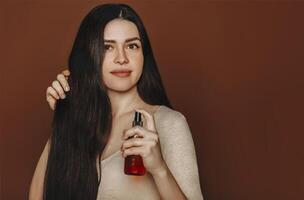 Studio portrait of happy satisfied woman holding her long healthy brown hair and showing at camera shampoo or conditioner photo
