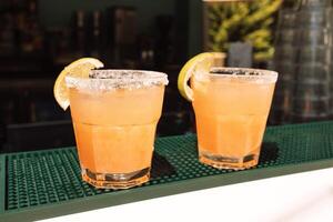 Two glasses with citrus cocktails on the bar. Chilled delicious drinks with lemon slices. photo