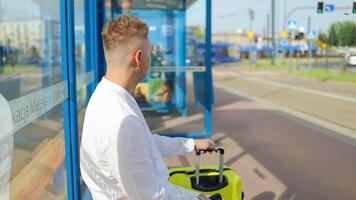 Handsome Tourist Caucasian business man traveler with bag and suitcase sit at public transport bus station waiting with mobile smart phone video