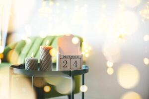 December 24 on wooden calendar standing on small table with burning candles in living room, selective focus. Christmas and New Year concept photo