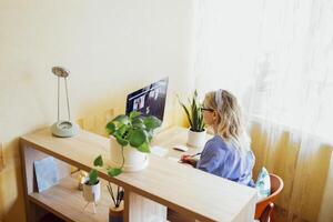 Young woman sits in front of computer monitor and talks via link. photo
