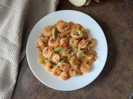 Udang asam manis or Sweet and sour prawns, made from fried prawns with tomato sauce on white plate on dark background. Chinese food photo