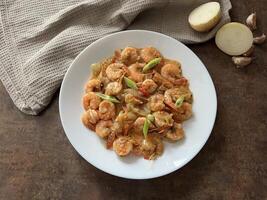 Udang asam manis or Sweet and sour prawns, made from fried prawns with tomato sauce on white plate on dark background. Chinese food photo
