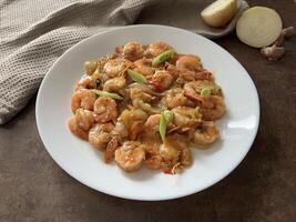 Udang asam manis or Sweet and sour prawns, made from fried prawns with tomato sauce on white plate on dark background. Chinese food photo