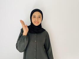 Indonesian woman with hijab smiling and looking at camera while rise her hand show something isolated on white background photo