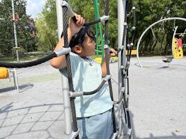 A young Asian little girl climbing on a rope in the playground. Happy kids concept. photo