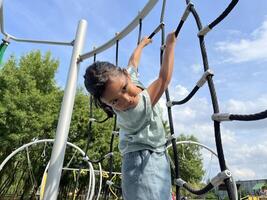 A happy young Asian little girl bravely climbing on a rope in the playground. Childhood concept. Down view photo