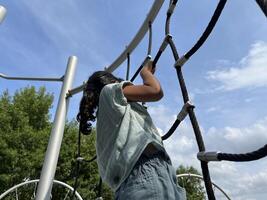 A young Asian little girl climbing on a rope in the playground. Rear view. photo
