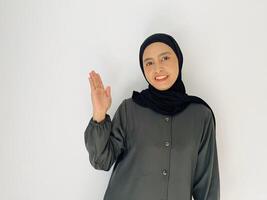 Indonesian woman with hijab smiling and looking at camera while rise her hand show something isolated on white background photo