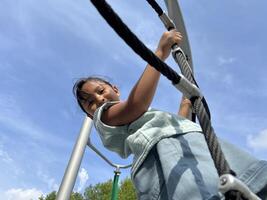 A happy young Asian little girl bravely climbing on a rope in the playground. Childhood concept. Down view photo