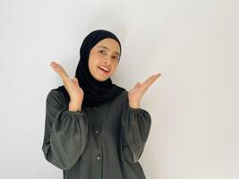 Indonesian woman with hijab smiling and looking at camera while rise her hand show something isolated on white background photo
