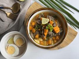 Beef soup is made from beef broth cooked with spices served with vegetables such as potatoes, carrots, spring onions, lime and boiled eggs. Perfect for articles, recipe books and creative production photo