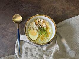Bubur ayam is an Indonesian chicken congee. It is rice congee cooked with coconut milk served with shredded chicken meat chopped scallion, boiled egg, topped with yellow chicken broth photo