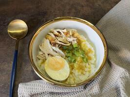 Bubur ayam is an Indonesian chicken congee. It is rice congee cooked with coconut milk served with shredded chicken meat chopped scallion, boiled egg, topped with yellow chicken broth photo