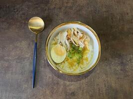Bubur ayam is an Indonesian chicken congee. It is rice congee cooked with coconut milk served with shredded chicken meat chopped scallion, boiled egg, topped with yellow chicken broth photo