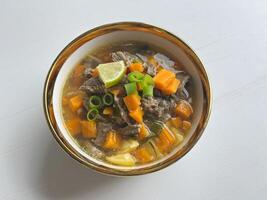 Beef soup is made from beef broth cooked with spices served with vegetables such as potatoes, carrots, spring onions, lime and boiled eggs. Perfect for articles, recipe books and creative production photo