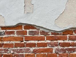 Texture of an old brick wall with fallen plaster and peeling wall paint. Background of a shabby building surface photo