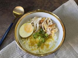 Bubur ayam is an Indonesian chicken congee. It is rice congee cooked with coconut milk served with shredded chicken meat chopped scallion, boiled egg, topped with yellow chicken broth photo