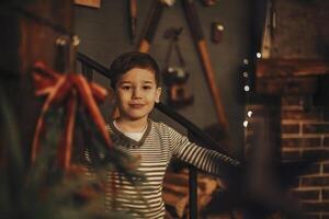 Cute little boy smiling at camera while standing indoor of cozy rustic farmhouse in Christmastime photo