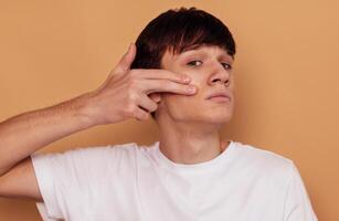 A young guy applies a moisturizing gel to his cheeks for problem skin. A serious teenager in a white T-shirt takes care of his face. photo