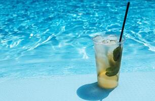 Delicious ice drink with lime, lemon and mint on the side of the pool. Tasty fresh mojito on the background of clear blue water. photo