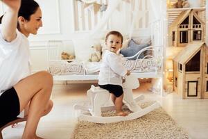 An attractive brunette woman is having fun with her sweet son at home. Adorable mom and cute baby are playing in the bedroom. Happy family. photo