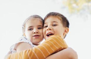 Little cute kids in casual clothes hug each other tightly. Pretty girl and boy are smiling and looking at the camera. photo